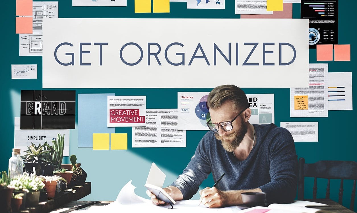 Person working at a desk with notes and charts, under a large 'Get Organized' sign, emphasizing productivity and planning.