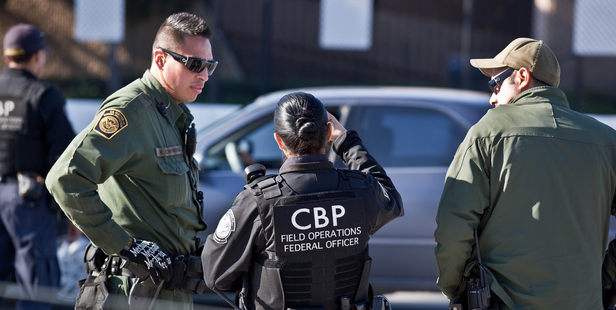 CBP officers in tactical gear during a field operation, standing and discussing near a parked vehicle.