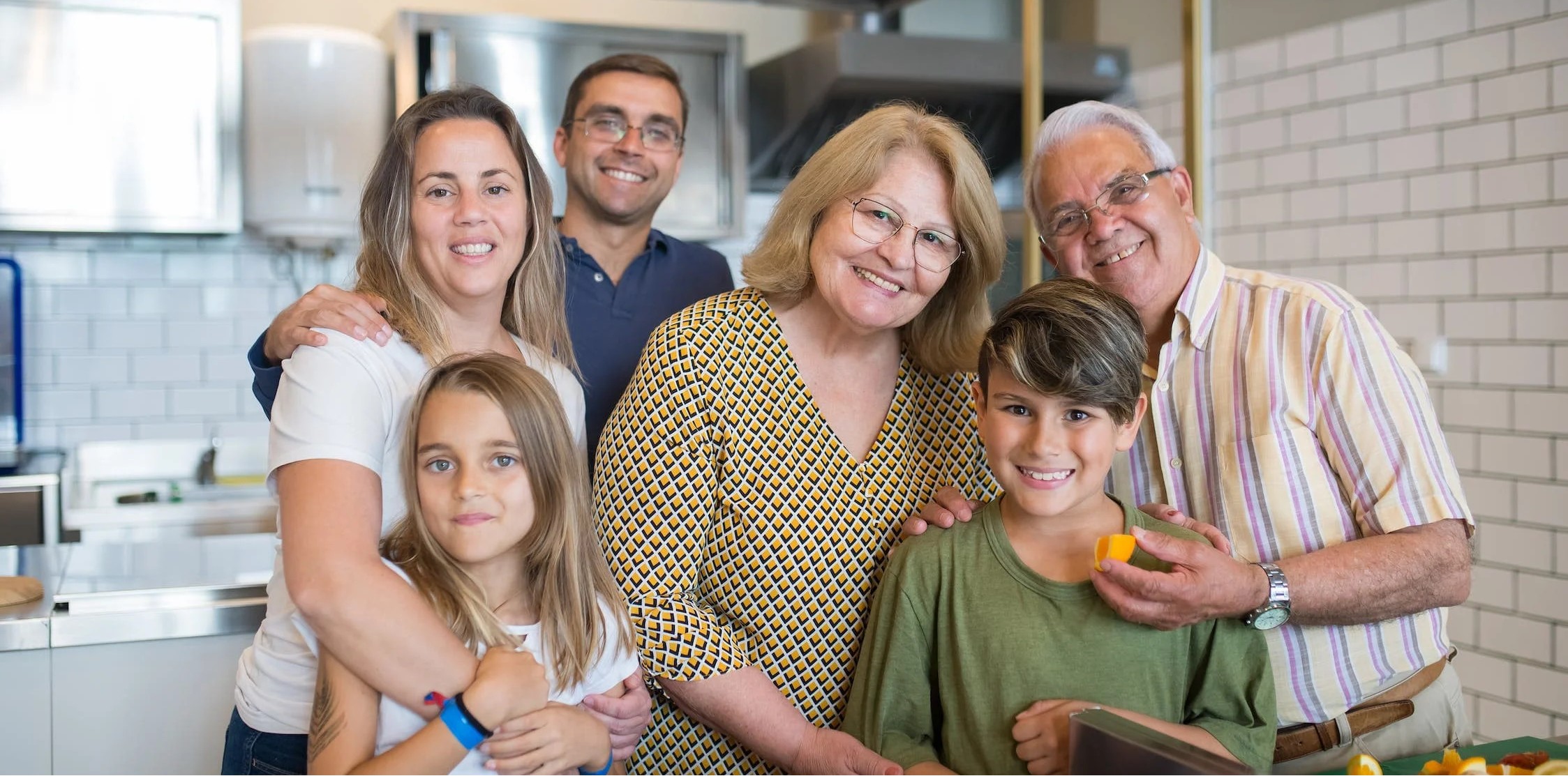 A happy multi-generational family smiling together in a kitchen setting.