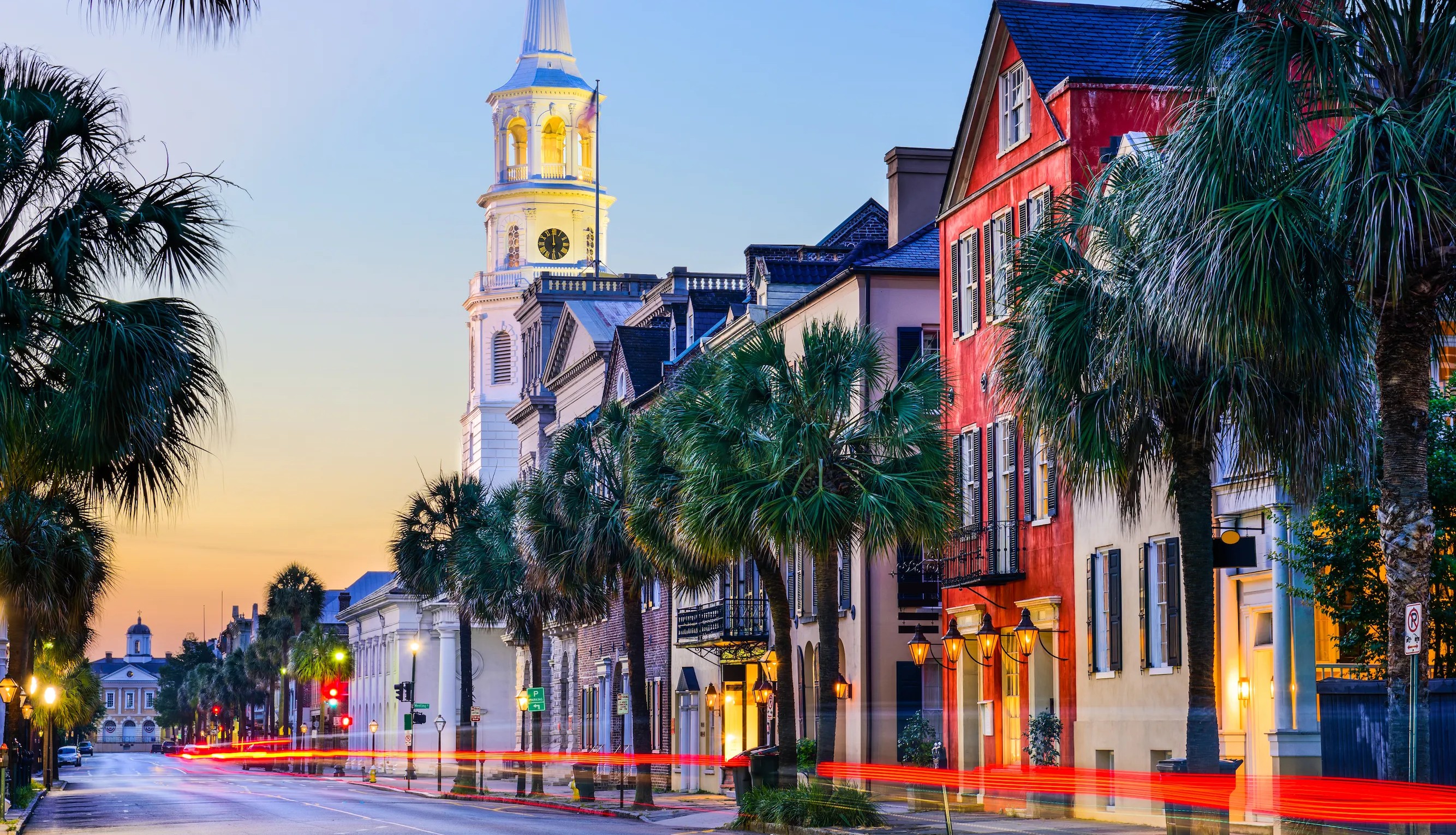 Colorful historic buildings and palm trees line a vibrant street at sunset, with a clock tower visible.